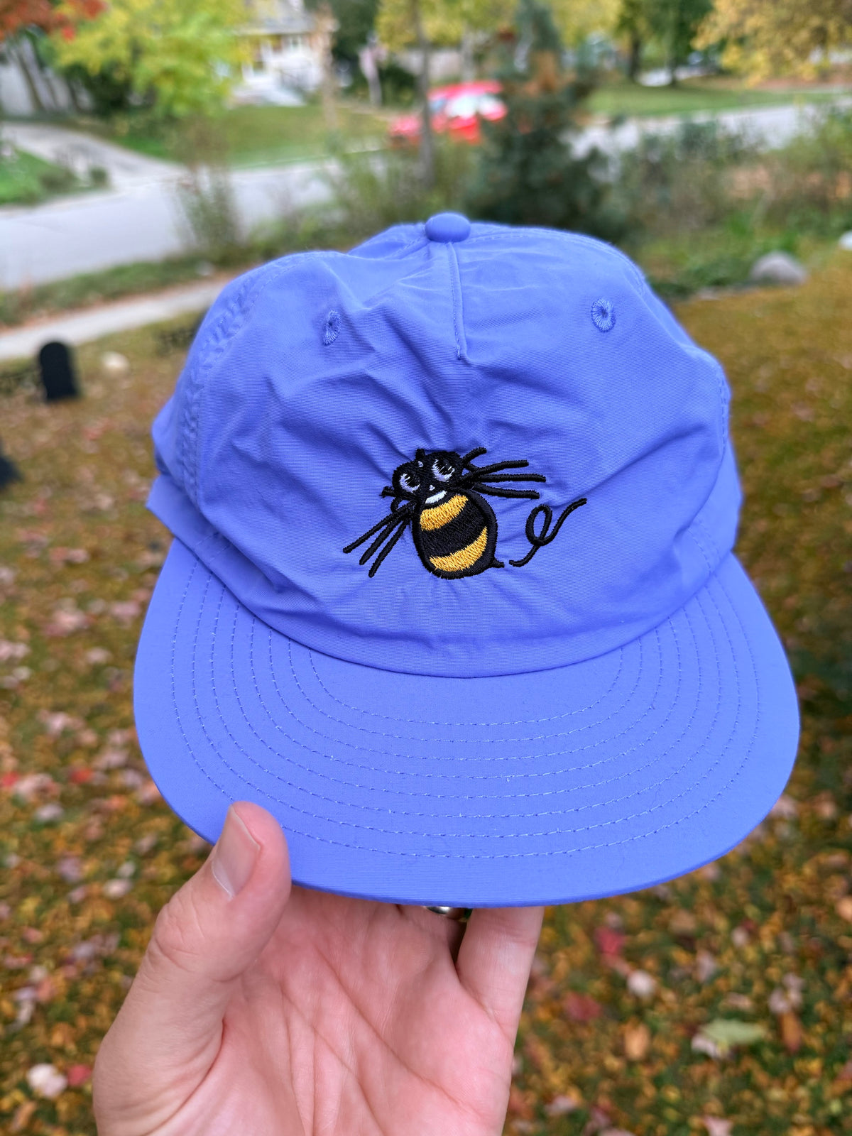 Hand holding the lapis blue Hudson Soft Bee Surf Cap outdoors, with the black and yellow Hudson Soft bee embroidered on the front
