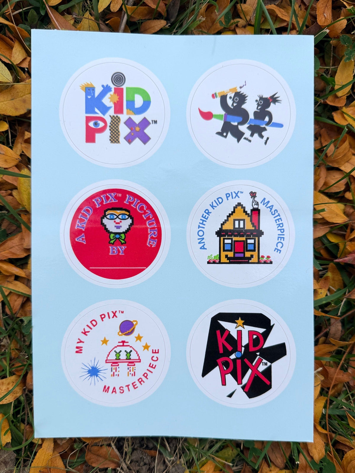 Kid Pix Sticker Sheet on fall leaves: six round stickers including the Kid Pix logo, A Kid Pix Picture By and two Masterpiece stickers