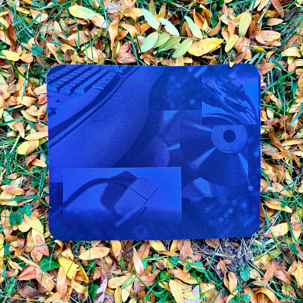 Windows 95 Setup Mouse Pad lying flat on fall leaves and grass, showing the dithered blue collage of a keyboard, mouse, cables and a CD